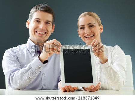 Young happy business people on a meeting. Male and female. Pointing on a blank computer tablet screen. Place for your text or photo.