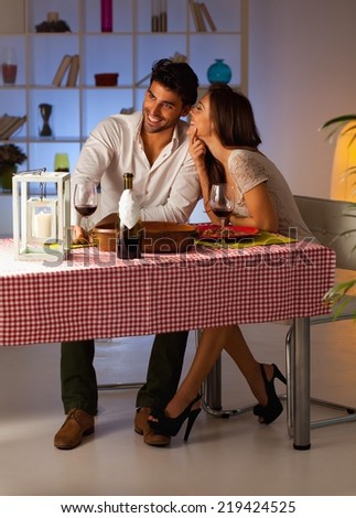 Romantic couple having dinner at home. Man whispering to woman.