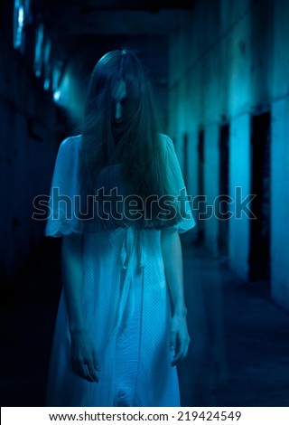 Scary woman with hair over her face standing in a dark hallway.
