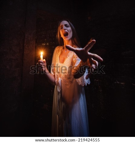 Scary woman standing in a dark hallway with lighten candle and screaming.
