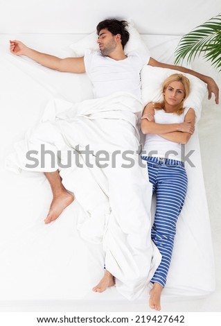 Woman is trying to fall asleep while man is taking most of the space in bed.
