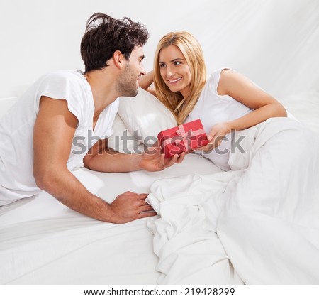 Boyfriend giving a present to his girlfriend in bed at home.
