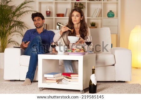 Couple sitting in the living room, having dinner and watching TV.