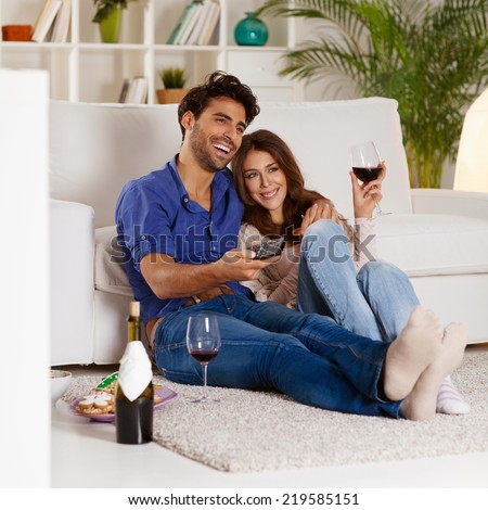 Couple sitting in the living room, having wine and watching TV.