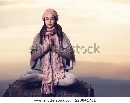 Young woman meditating in nature sitting on the rock.
