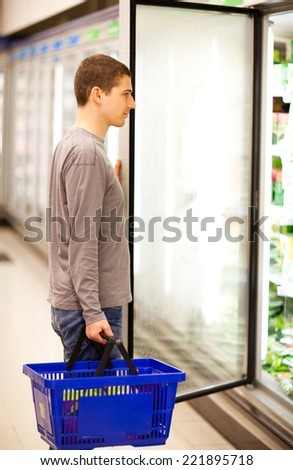 Young man standing by the open freezer in a supermarket.