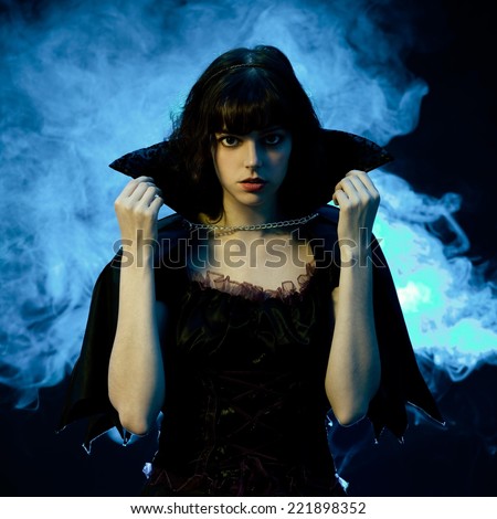 Scary woman in a Halloween costume with bat wings. Blue smoke in the background.