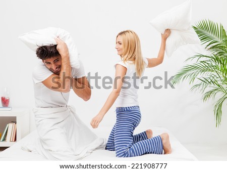 Romantic young couple enjoying pillow fight in bed at home.