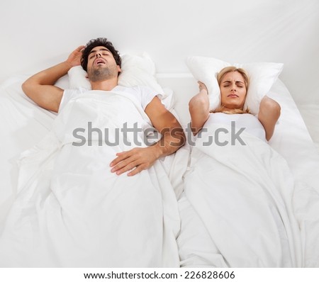 Woman is trying to fall a sleep while man is snoring.