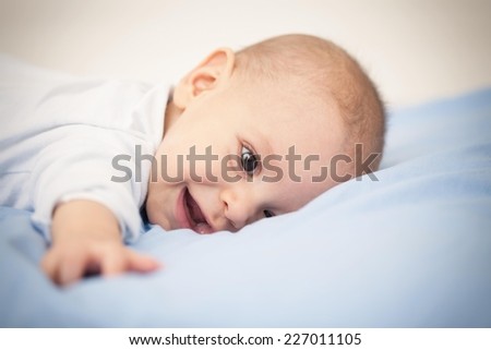 Cute six months old baby boy lying on a bed.