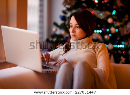 Young beautiful woman sitting on the sofa and sending Christmas e-mails.