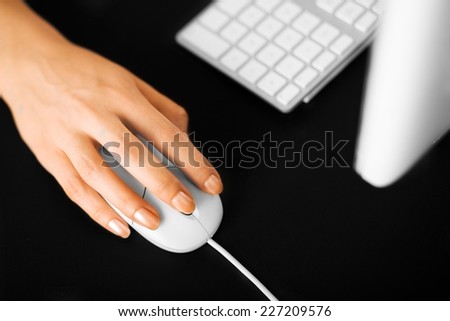 Female hand on a computer mouse, keyboard and monitor blured