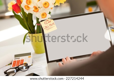 Man working on a laptop. Having reminder on his monitor to call mom for Mother\'s Day.