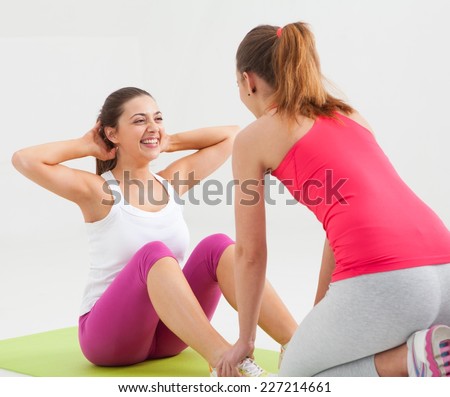 Young women doing sit-ups in a studio. Helping each other.