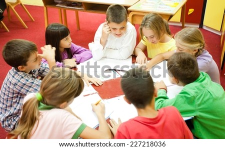 Group of elementary school children sitting around the table in the classroom and reading.  NOTE: All the drawings and artwork in the classroom are made by children.