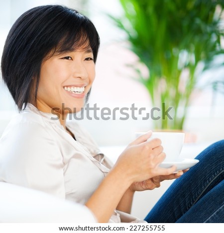 Beautiful asian woman drinking coffee on the sofa and chatting with friend.