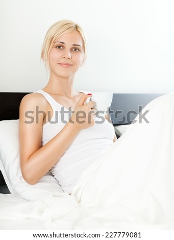 Young woman sitting in bed drinking tea or coffee.