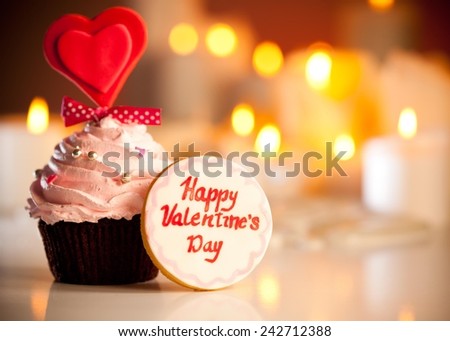 Cute Valentine\'s cookie with Happy valentine\'s day written on it next to Valentine\'s cupcake.