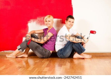 Young caucasian couple sitting on the floor and smiling in front of partially painted wall