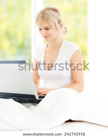 Beautiful girl in bed working on laptop - window in the background.
