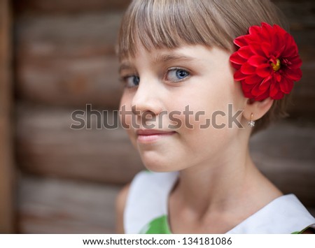 Attractive seven-year old girl with a red flower in her hair in front of a log wall