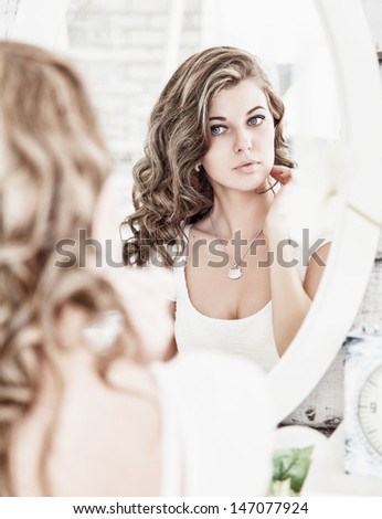 Young beautiful woman looking at her face in the mirror