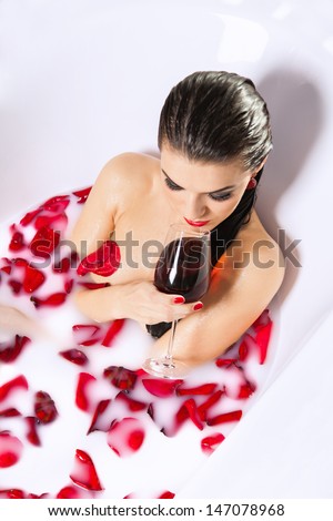 Attractive naked girl enjoy a glass of wine in bath with milk and rose petals. Spa treatments for skin rejuvenation and full relaxation
