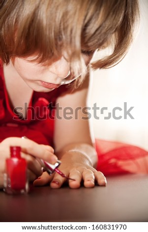 Four-year girl in a red dress with interest paint on nails with nail polish. Close-up view.