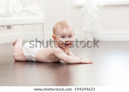 Happy seven month old baby girl crawling on a hardwood floor in living room