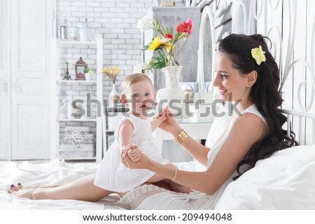 Good morning! Mother playing with a year-old daughter on the bed in the bedroom