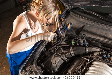 Girl checks the oil level with dipstick in their own broken car