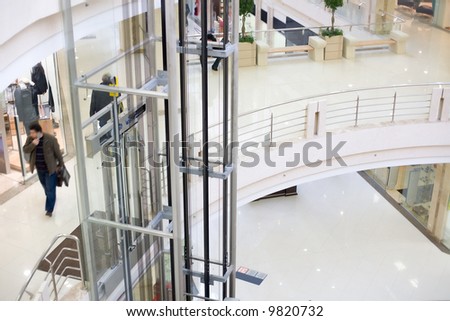 Modern glass elevator in the mall. Walking peoples in motion blur