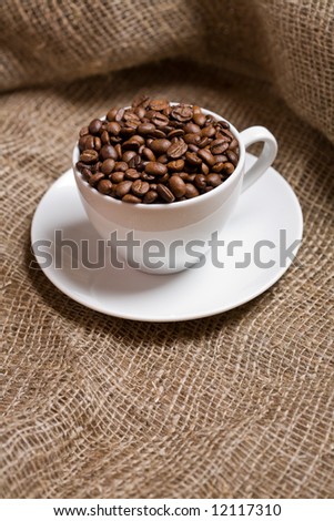 Cup with freshly roasted coffee beans on sackcloth. Shallow depth of field. Focus on the beans.