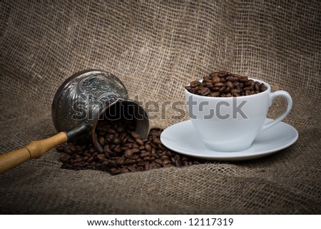 Cezve and cup with freshly roasted coffee beans on sackcloth. Focus and light accent on center of image