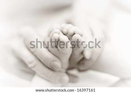 Mother gently hold baby leg in hand. Slightly toned black & white image with soft focus on babie\'s foot