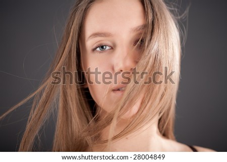 Portrait of attractive girl with fly-away hair on the wind. Over gray