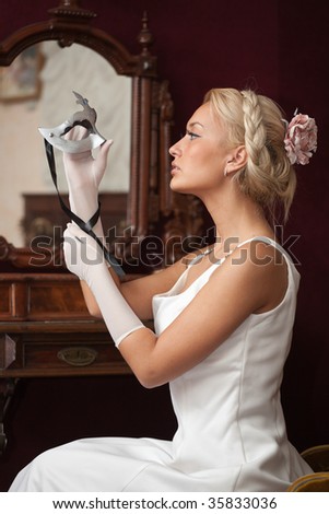 Portrait of beautiful young woman in vintage interior holding venetian carnival mask