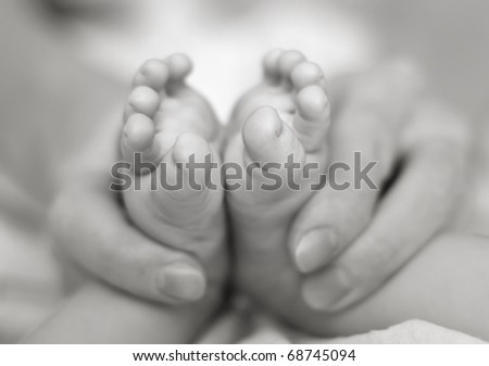 Mother gently hold baby legs in hand. Slightly toned black & white image with soft focus on babie\'s foot