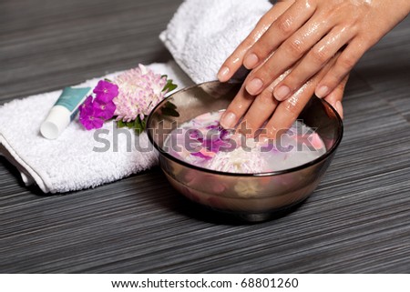 Human hands in bowl with cosmetic oil and chrysanthemum flowers. Beauty treatment in spa salon