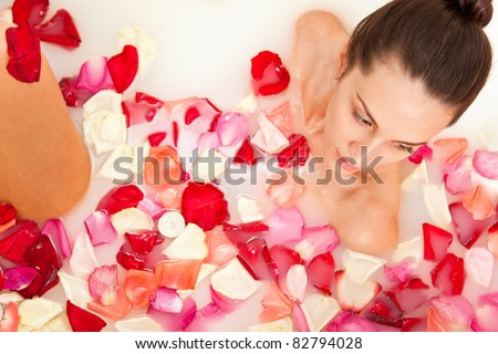 Attractive naked girl enjoys a bath with milk and rose petals. Spa treatments for skin rejuvenation