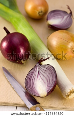 leeks, red onion, yellow onion, a knife on a wooden board