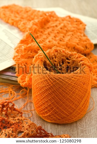 orange ball of yarn, a hook, a knitted fabric