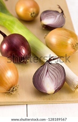 leeks, red onion, yellow onion on a wooden board