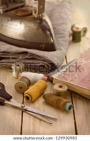 spools of thread, scissors, iron, old books on a wooden board (vintage)