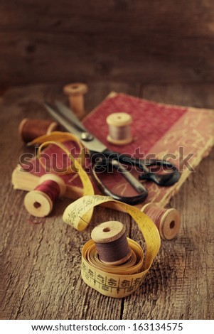 Old spools of thread, measuring tape, scissors on a wooden background