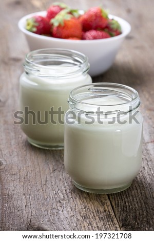 homemade yogurt in a glass jar and strawberry on a wooden background