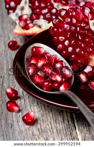 old spoon with pomegranate seeds, slices of pomegranate on a wooden background