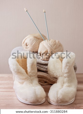 Pair of warm winter sheepskin slippers (alpaca), wool yarn, knitting needle  on a pile of warm woolen clothes (Selective focus)