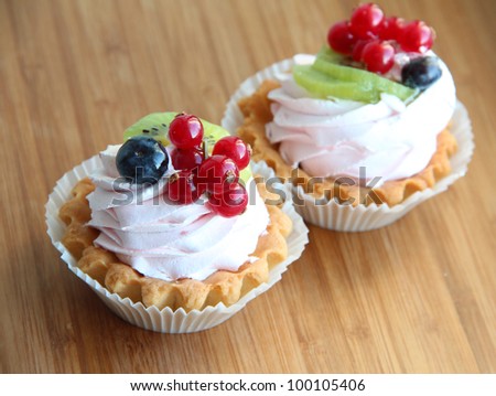 Two cute fancy cakes/cupcakes with creamy topping and berries -- red currants and blueberries on top against a wooden background
