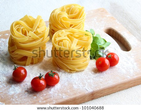 Composition made in colours of Italian flag: three portions of raw tagliatelle pasta along with cherry tomatoes and herbs on a cutting board
